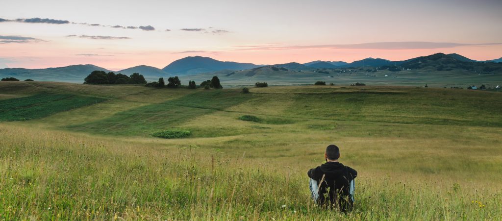 man meditating in a field with mountains in the background