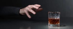 man with untreated alcoholism reaches out for a glass of liquor