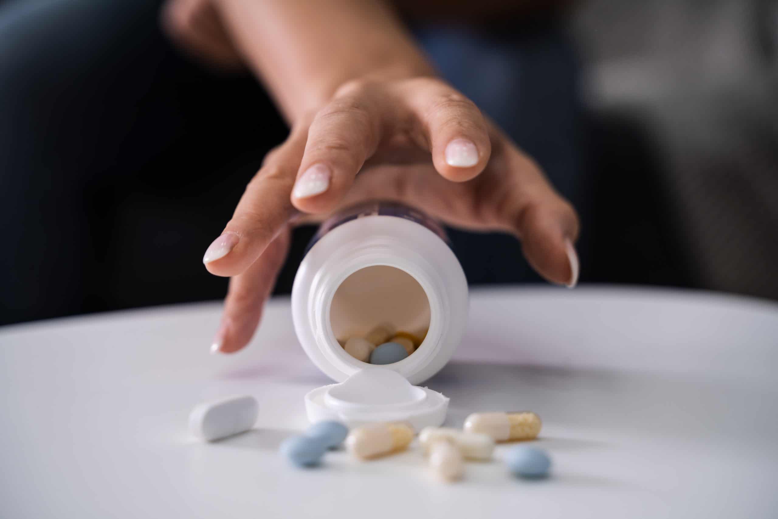 woman reaching for pill bottle full of addictive drugs