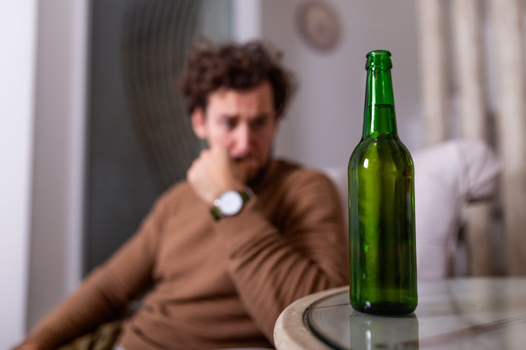 man is tempted to return to poor coping habits and thinks about drinking beer next to him
